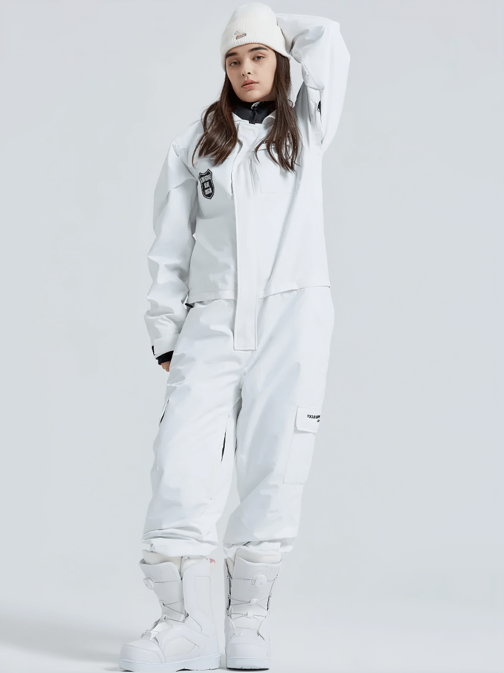 Woman modeling a white windproof snowboarding one-piece suit with beanie, showing practical design and stylish embroidery accents.