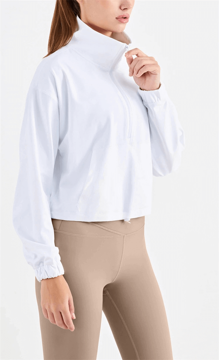 Woman wearing a white workout sports sweatshirt, showing the v-neck and pocket design, paired with beige fitness leggings.