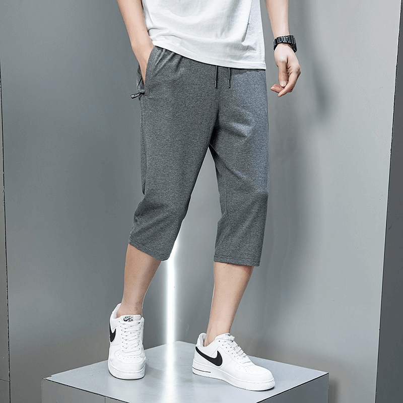 Casual men's sportswear: breathable cotton breeches with zip pockets and drawstring closure, perfect for outdoor activities. Model wearing grey shorts.