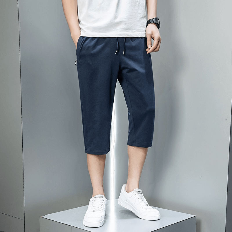 Man wearing navy breathable cotton breeches with zip pockets and drawstring, standing casually against a gray background.