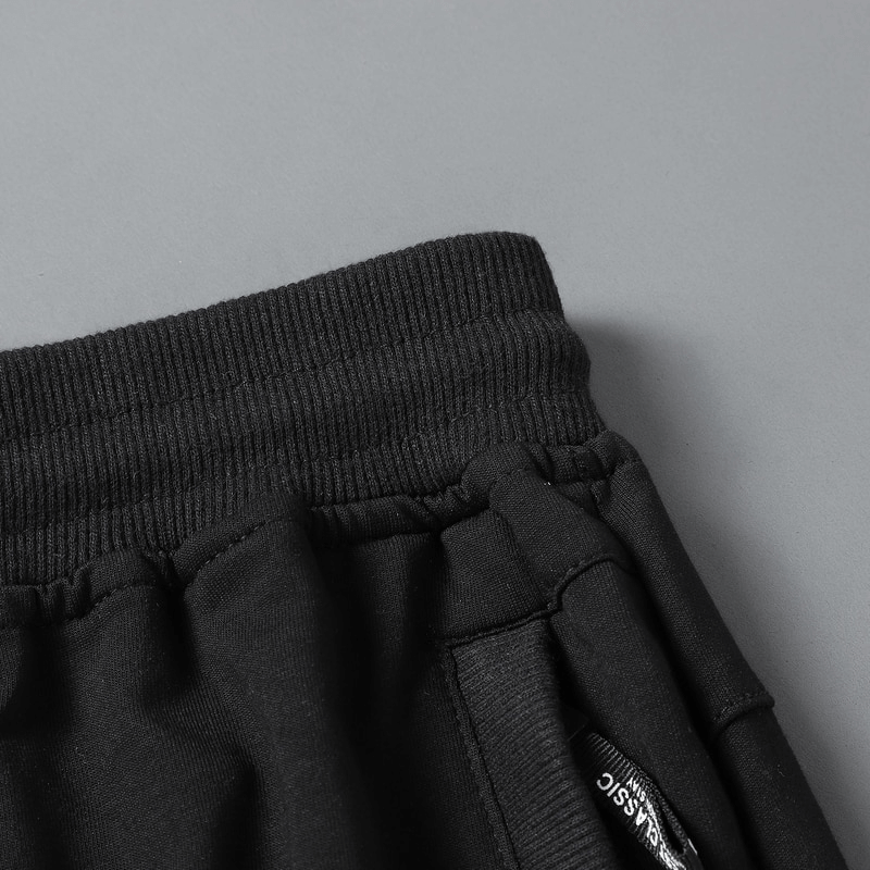 Close-up of black breathable cotton breeches with zip pocket and ribbed waistband, designed for casual men's sportswear.