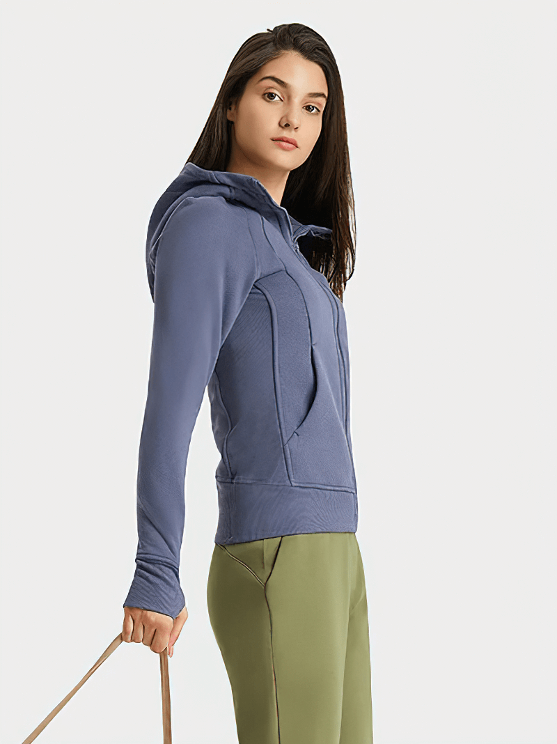 Woman wearing a zip-up athletic fleece hoodie, SF1919, in blue, standing stylishly with full-length sleeves and pockets visible.