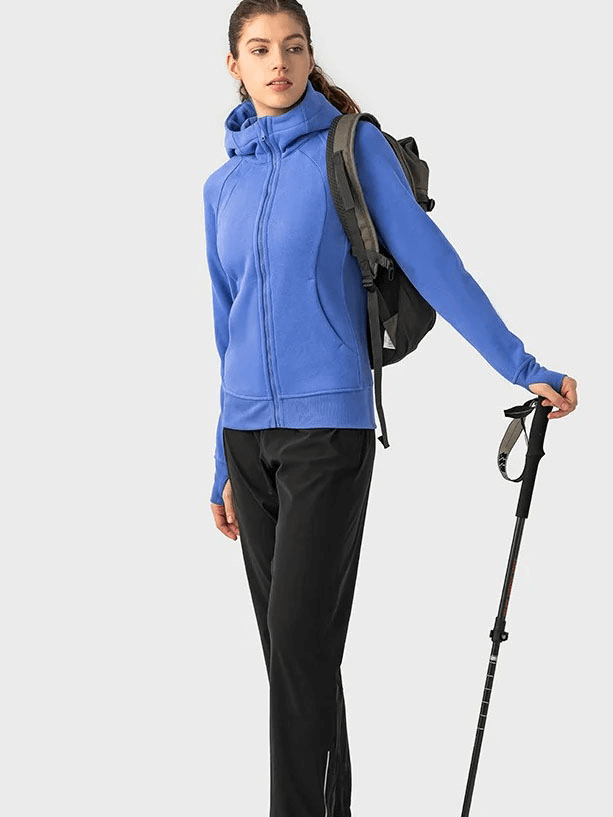 Woman wearing a blue zip-up athletic fleece hoodie with backpack and hiking pole, showcasing outdoor sportswear style.