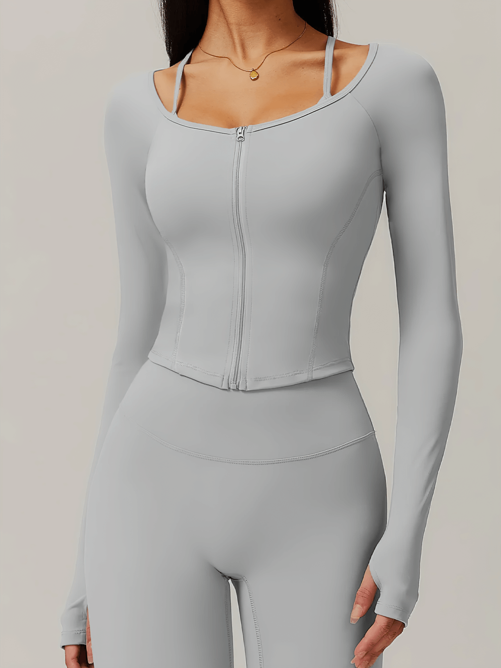 Woman wearing gray zip-up long-sleeve yoga top with thumbholes, showcasing sleek activewear for gym or yoga sessions.