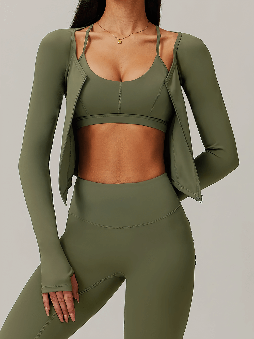 Olive green zip-up long-sleeved yoga top with thumbholes, worn by a woman, perfect for workouts, providing style and functionality.