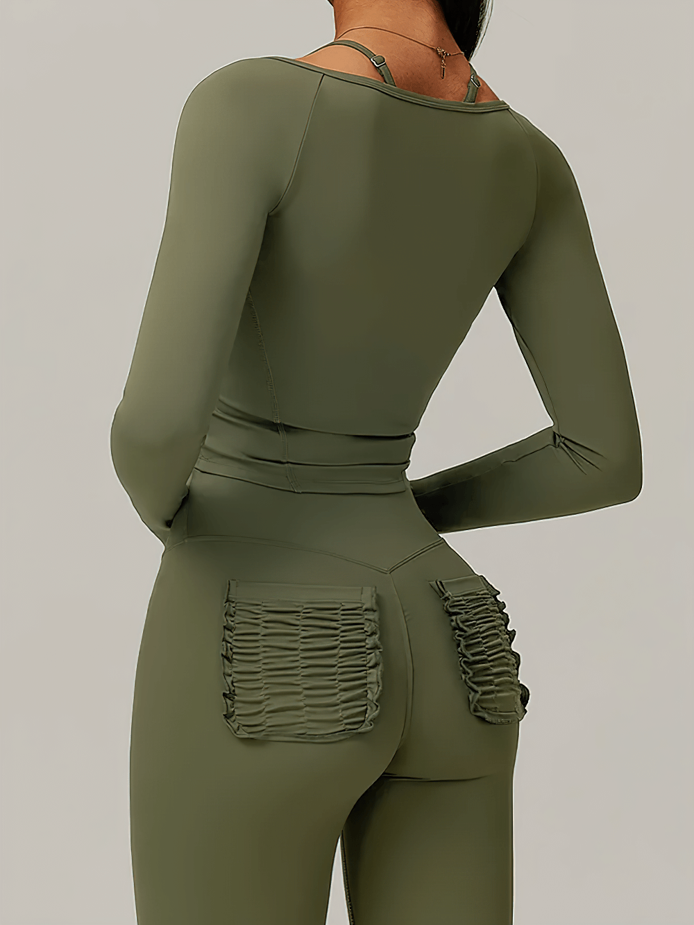 Back view of woman in olive green zip-up long-sleeve yoga top and leggings, showcasing figure-hugging fit and stylish design.