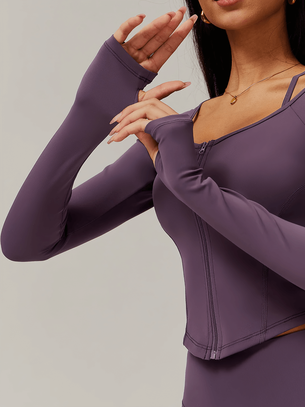 Stylish woman in a sleek zip-up long-sleeve yoga top with thumbholes, showcasing quick-dry fabric in a figure-hugging fit.