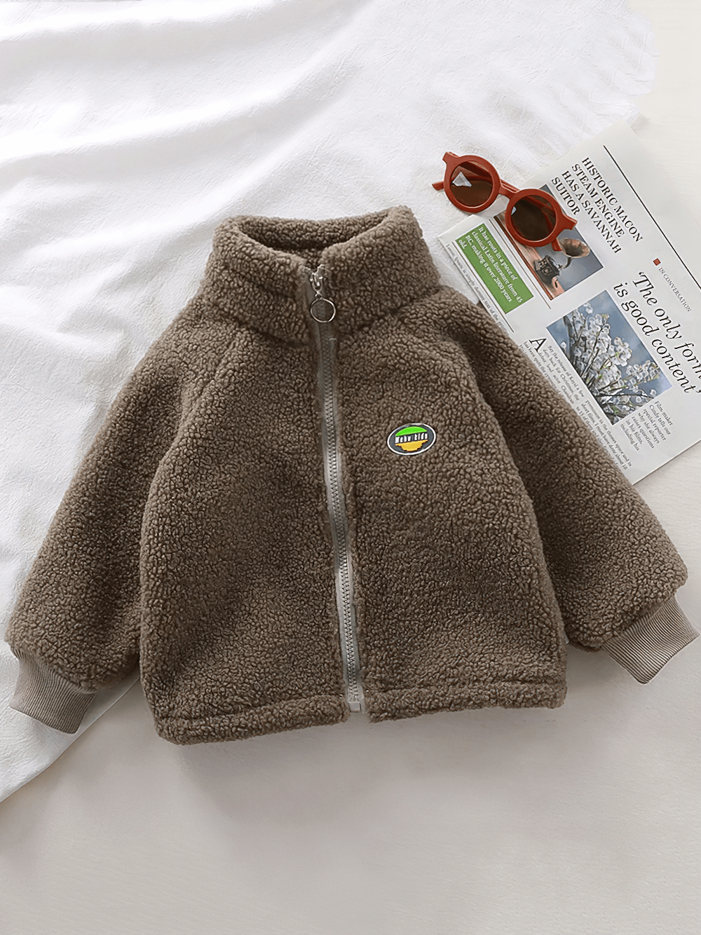 Zip-Up Sherpa Fleece Jacket with Stand Collar - SF3529, plush kids' winter coat on display with sunglasses and a newspaper.
