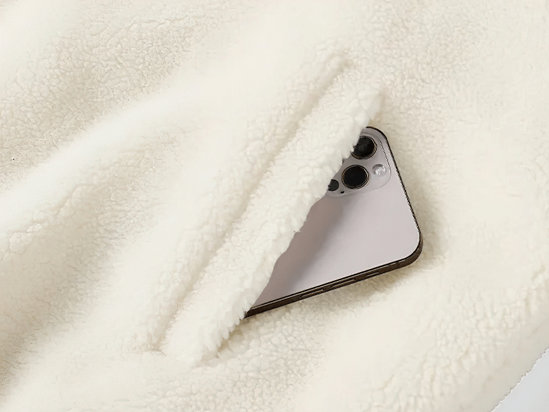 Close-up of a fluffy white fleece jacket pocket holding a smartphone, showcasing the jacket's practicality and style. Perfect for winter fashion.