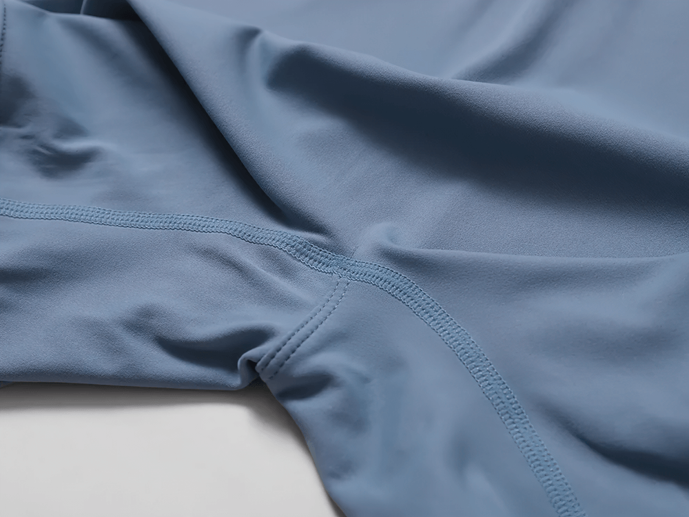 Close-up of blue stretch fabric on women's zippered workout romper, showcasing seamless stitching and smooth texture.