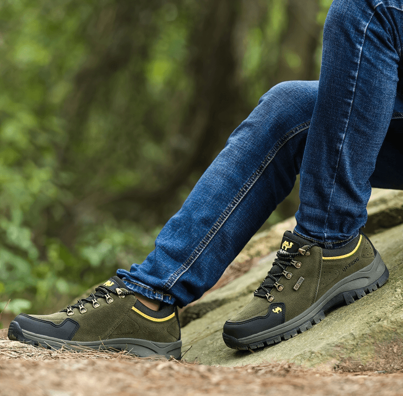 Person wearing athletic non-slip waterproof hiking shoes SF0246, sitting on a rock in a lush outdoor setting.