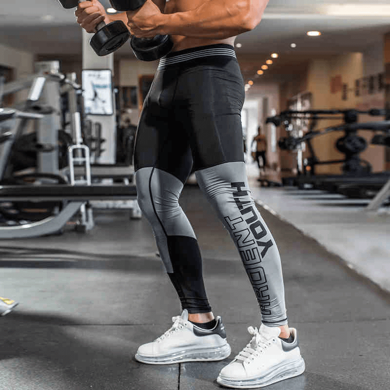 Man wearing quick-drying athletic compression tights, ideal for running and fitness, showcasing gray/black print design in a gym setting.