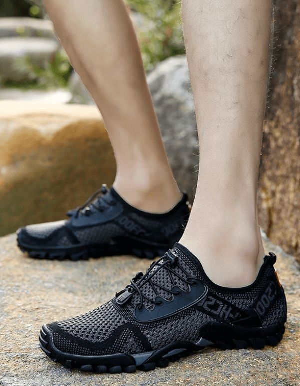 Black breathable elastic camping shoes for men with mesh upper, durable rubber outsole, and EVA insole on rocky outdoor terrain.