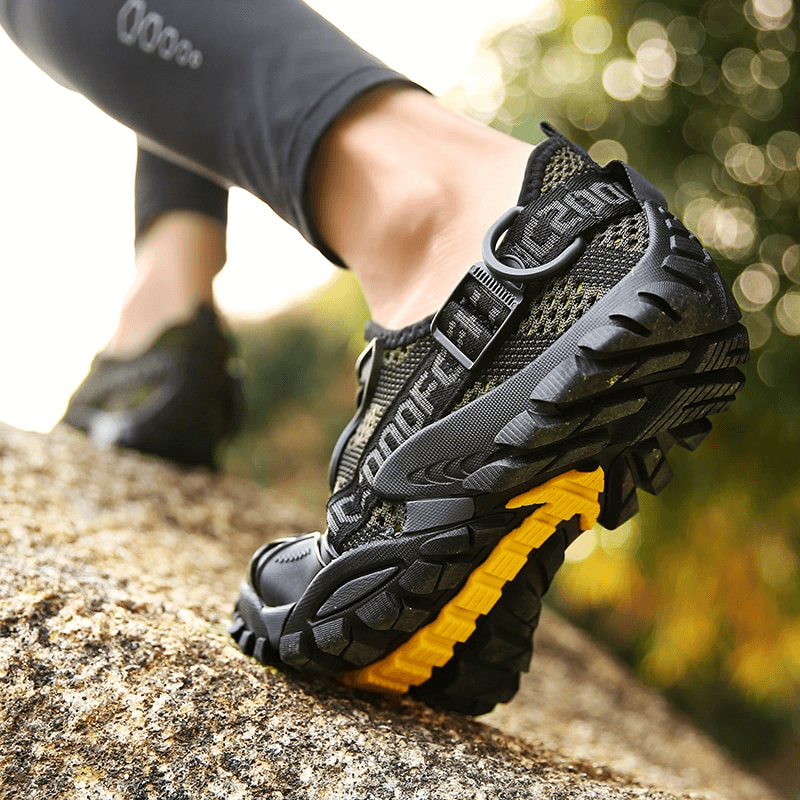 Close-up of breathable mesh trekking shoe on rocky terrain, showcasing durable rubber outsole for enhanced traction during outdoor activities.
