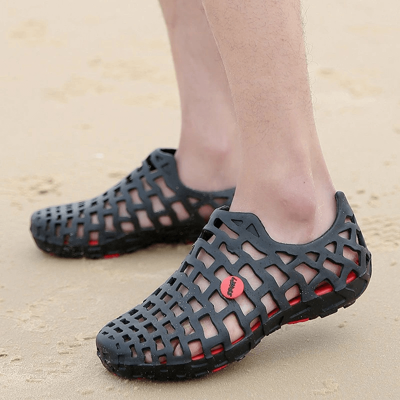 Person wearing breathable rubber beach slippers on sandy beach; unisex water shoes with synthetic upper and durable rubber outsole.