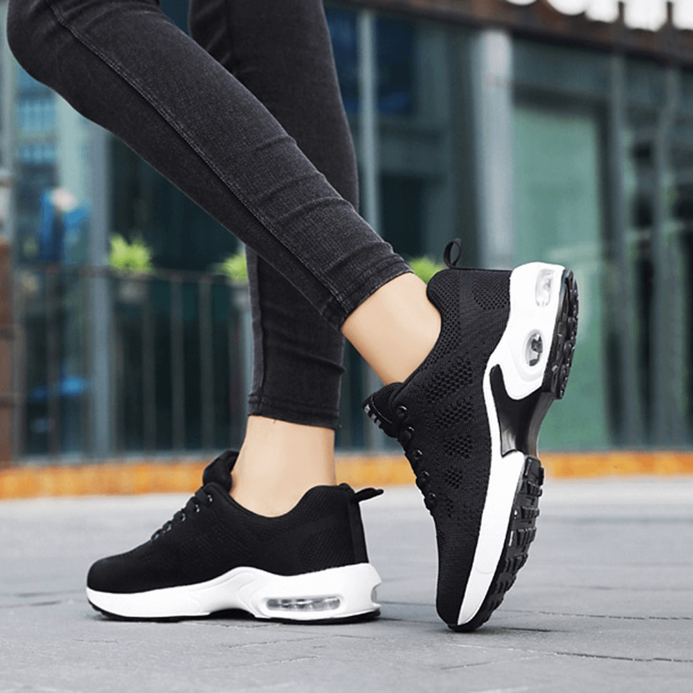 Person wearing breathable, wear-resistant black running shoes with cushioned soles walking outdoors.