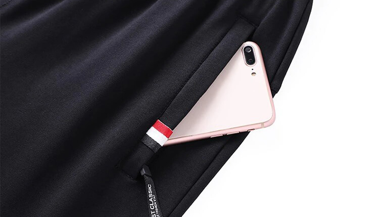 Close-up of men's black cotton sweatpants with pocket holding a smartphone, showcasing casual style and practicality with elastic waistband.
