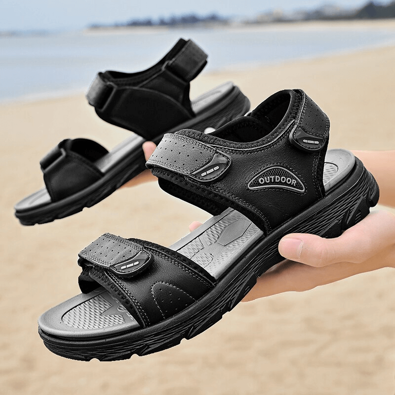 Black genuine leather sandals with soft soles perfect for hiking, trekking and casual wear, held at a beach setting.
