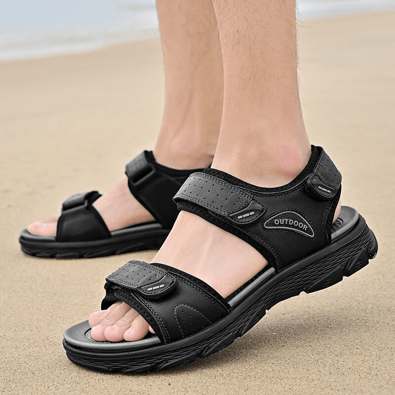 Man wearing black genuine leather hiking sandals on a sandy beach, showcasing comfortable and durable design for outdoor activities.