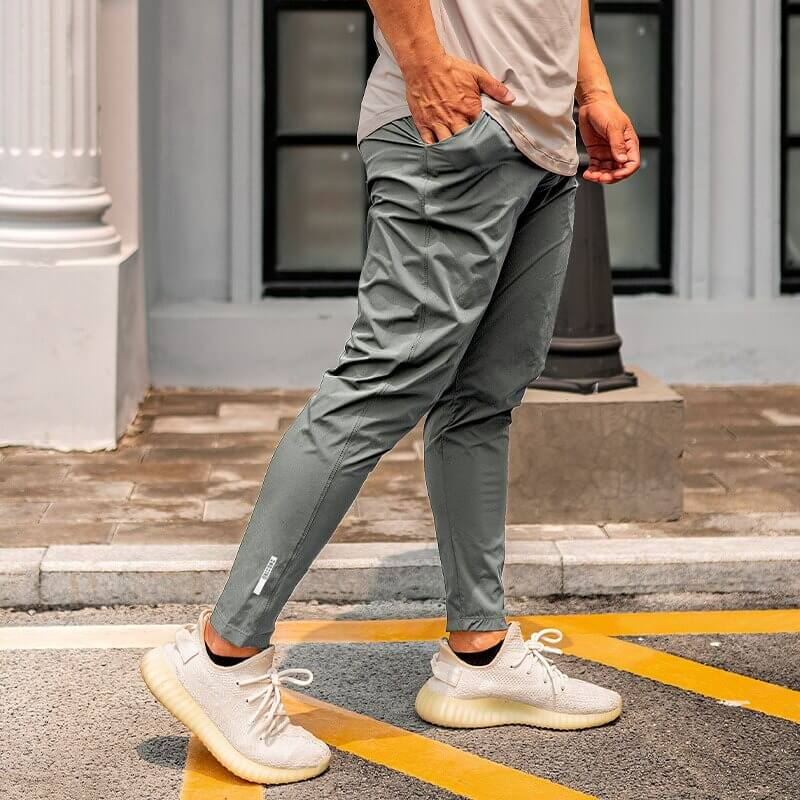 Man wearing gray casual male long sweatpants, ideal for running, with white sneakers and a casual shirt, street background.