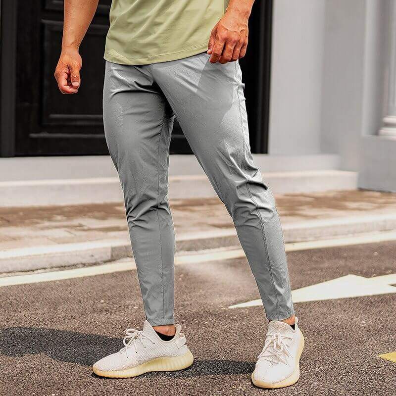 Casual male wearing long grey sweatpants for running; full-length design with elastic waist, made of polyester and spandex.