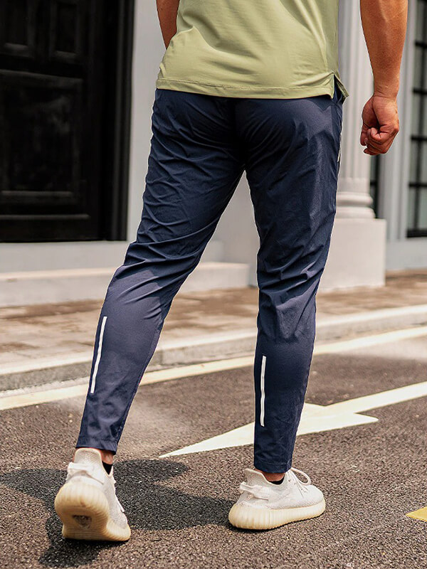 Man wearing navy sports workout trousers, built for running, showcasing the full length and style, on a sunny street.