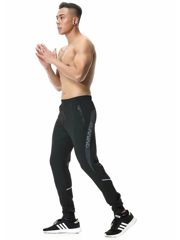Man wearing black casual running joggers with zipper pockets for men, featuring lightweight polyester and an elastic waistband.