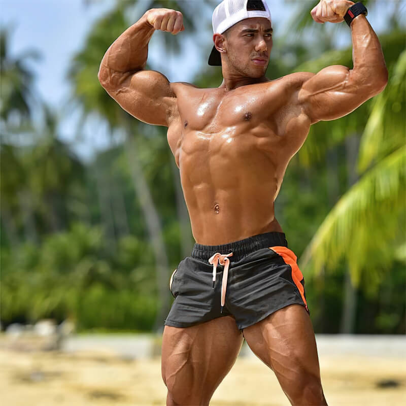 Man flexing muscles in Casual Training Drawstring Short Shorts for Men by the beach.