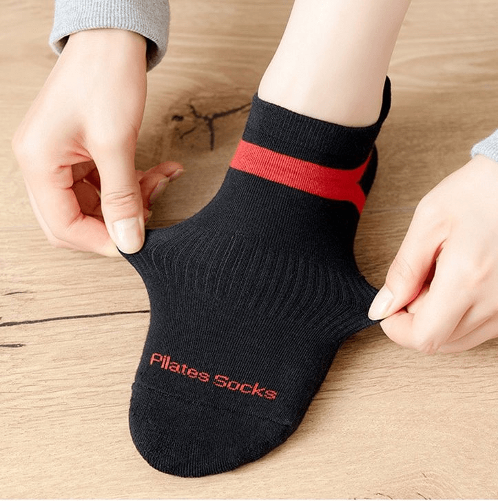 Person wearing black and red anti-slip compression socks perfect for yoga, showing flexibility and ergonomic design on wooden floor.