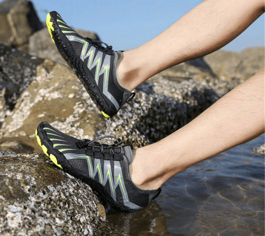 Person wearing drainage antiskid sole sports breathable swimming shoes, SF0557, standing on wet rocks by the water.