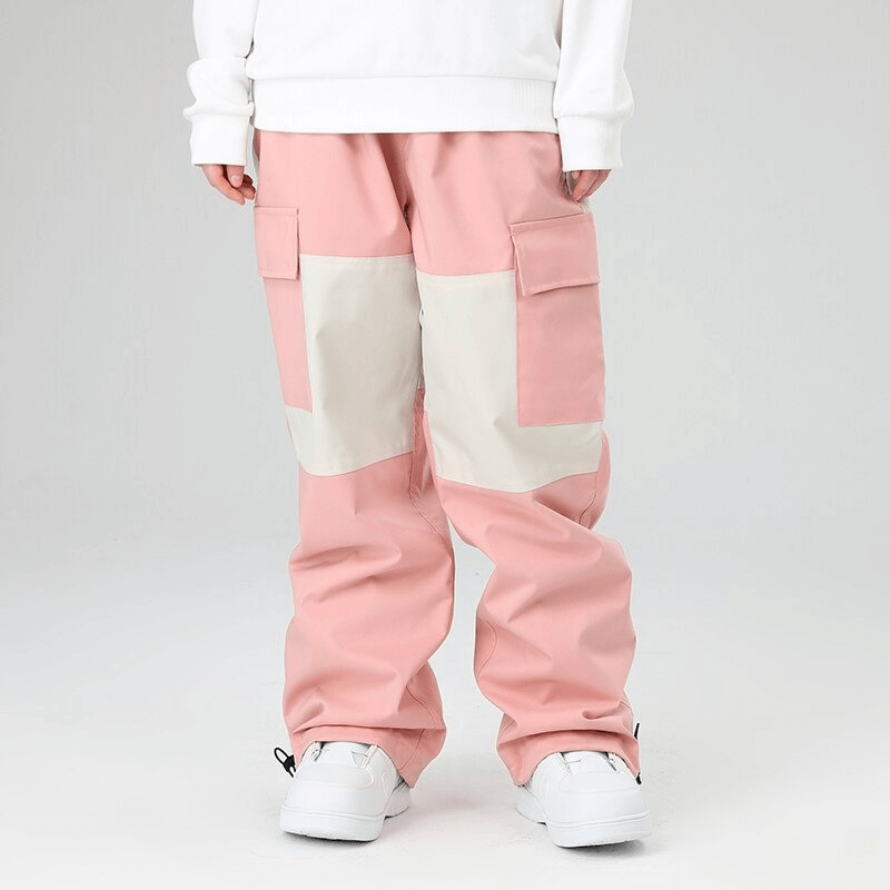 Unisex pink drawstring loose ski trousers with large pockets, ideal for snowboarding and extreme weather protection. Model wearing white sneakers.