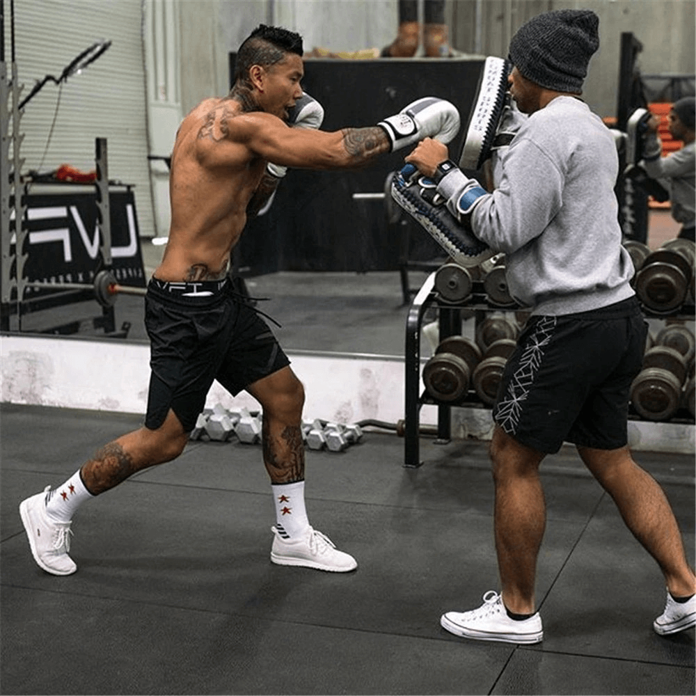Two men boxing in a gym, one wearing drawstring solid color running shorts and a beanie, showcasing gym clothing style.