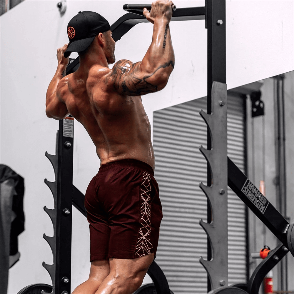 Man wearing drawstring solid color running shorts performs pull-ups in a gym. Ideal bodybuilding gym clothing for athletes. SF0352