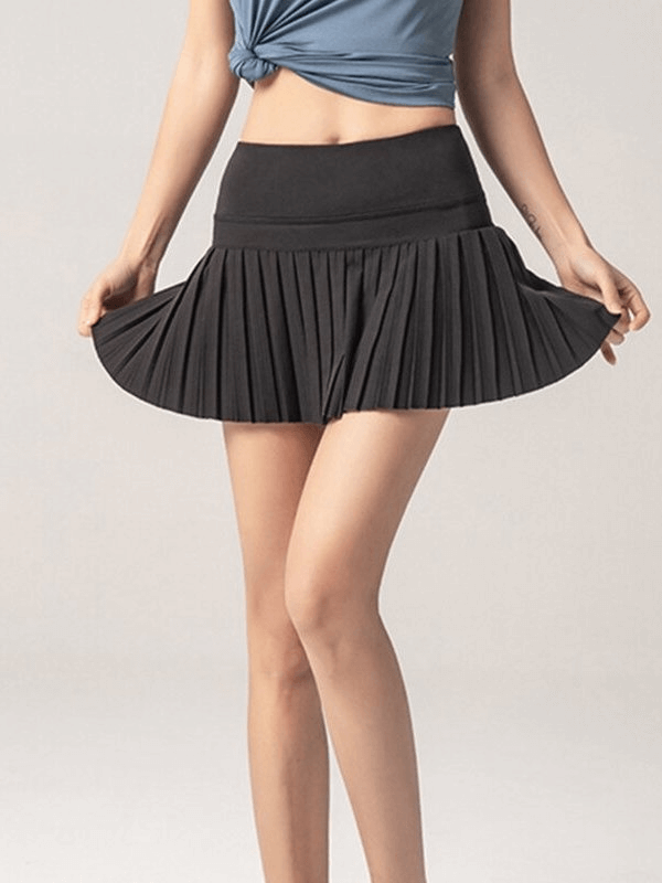 Woman wearing elastic pleated skirt-shorts for sports, showcasing comfort and style in breathable black polyester fabric.