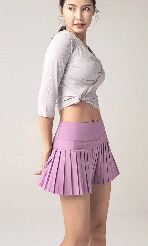 Woman wearing purple elastic pleated skirt-shorts, perfect for sports. Light grey top complements stylish activewear look.