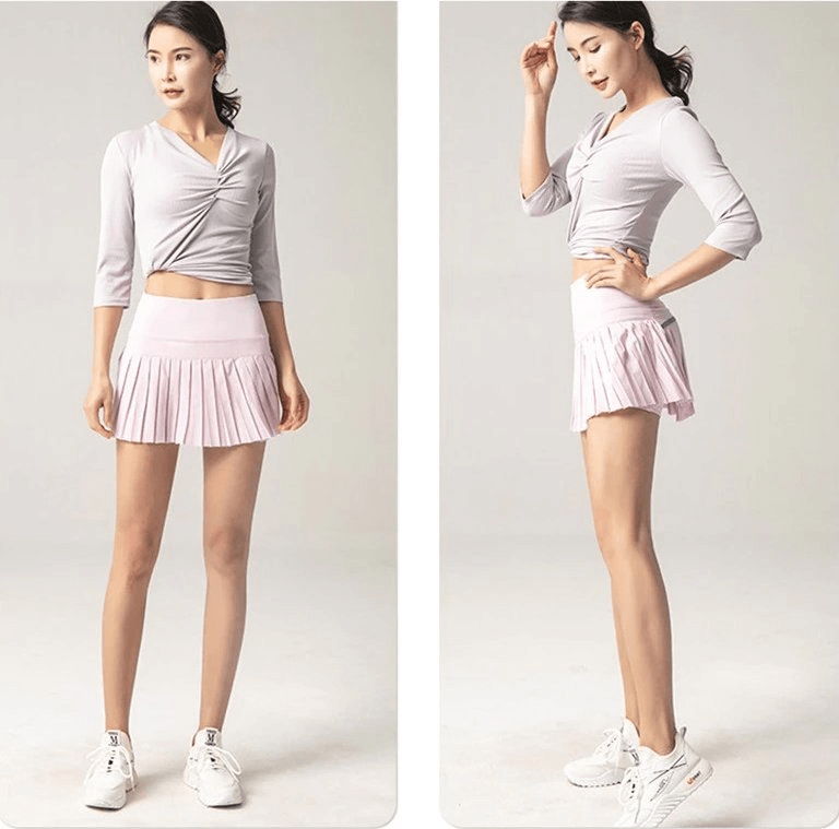 Woman in pink pleated skirt-shorts and gray top, modeling sporty and stylish women's activewear. Ideal for yoga or running.