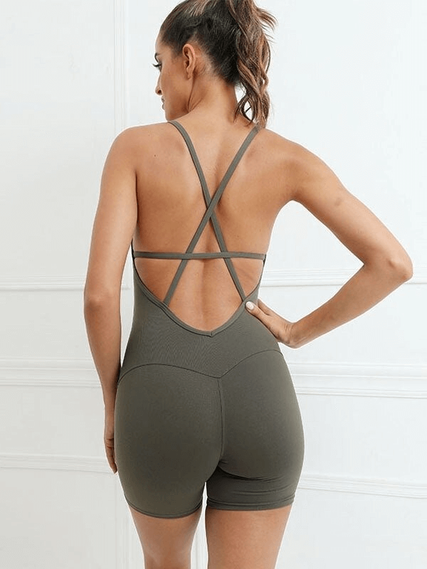 Back view of a woman wearing a green elastic sports short jumpsuit with an open-back design and crisscross straps.