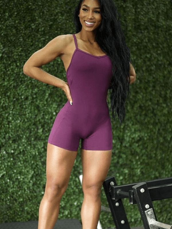 Woman in a purple elastic sports short women's open-back jumpsuit, emphasizing style and comfort, ideal for active workouts.