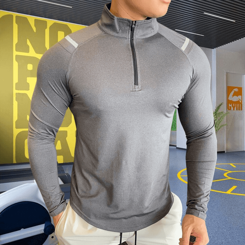 Men's gray slim sports top with long sleeves and zipper, featuring elastic microfiber material in a modern gym setting.