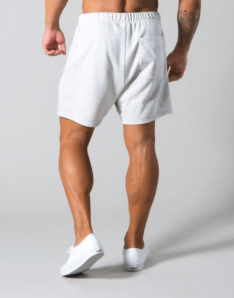 Man wearing elastic waist patchwork running shorts made of cotton blend in light gray, standing with casual white sneakers.