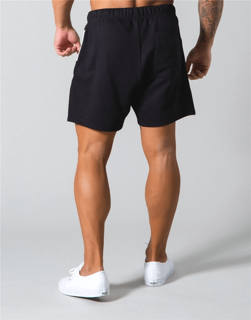 Man wearing black elastic waist patchwork running shorts with sneakers, showcasing comfort and style for gym workouts.