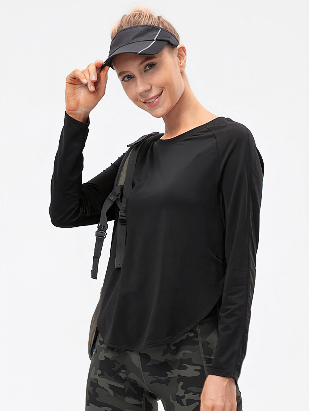 Woman in black long-sleeve yoga top with draped hem and split design, wearing cap and camo leggings, perfect for sports and workouts.
