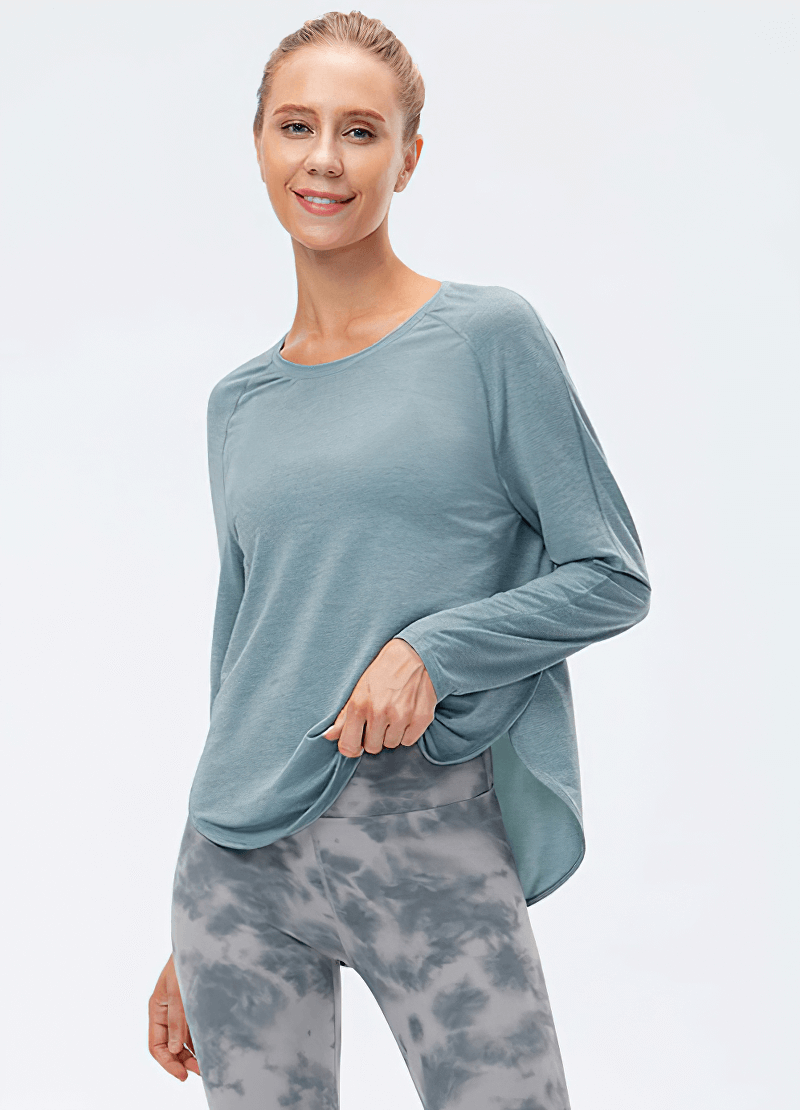 Light blue loose draped hem sports top with long sleeves, perfect for yoga. Worn by woman in patterned leggings, showcasing comfort and style.