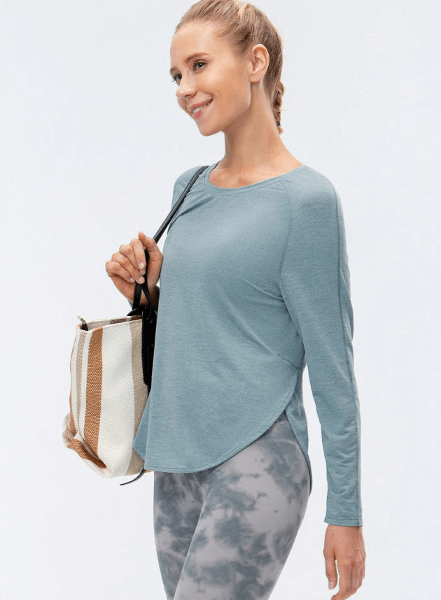 Woman wearing a blue long-sleeve sports top with draped hem and split design, ideal for yoga, paired with grey patterned leggings.