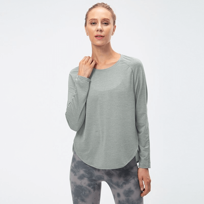 Woman wearing a grey long-sleeve yoga top with a draped hem and split design, perfect for workouts.