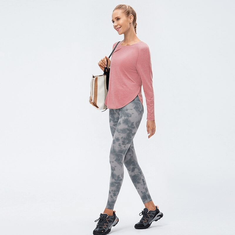 Woman in pink draped hem sports top and grey leggings, holding a bag, ideal for yoga and workouts.