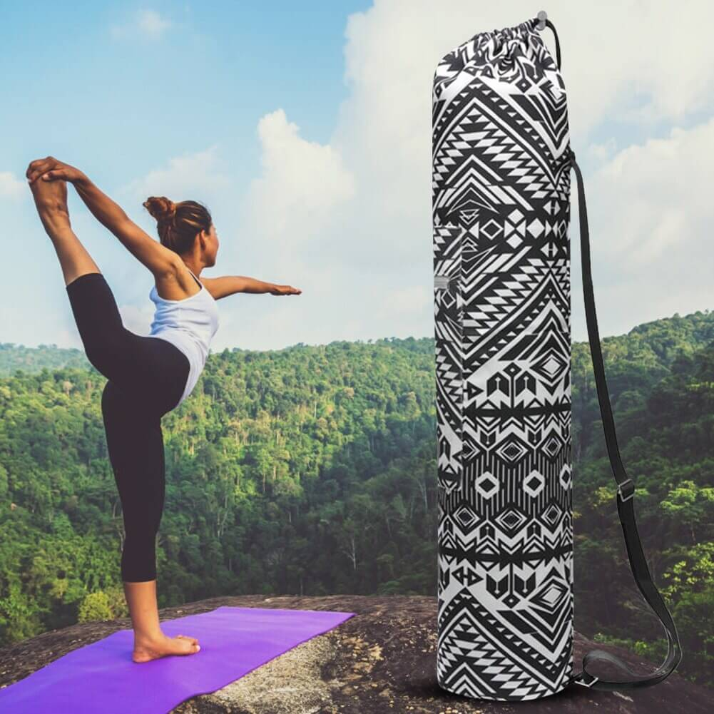 Woman practicing yoga near black and white aztec-patterned yoga mat bag with adjustable strap on a scenic outdoor backdrop.