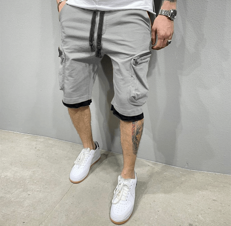 Men's cotton running shorts with zipper pockets, featuring flexible elastic waistband, worn by model with white sneakers.
