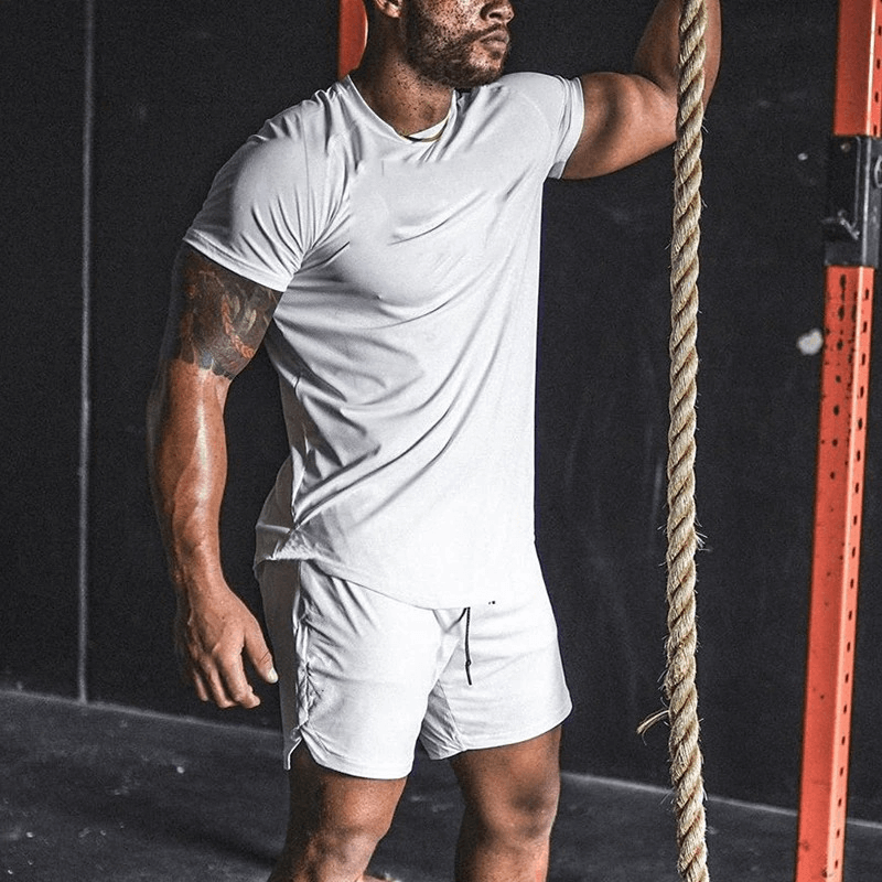 Man wearing a white O-neck short sleeve cotton jersey t-shirt and shorts, standing confidently in a gym setting.