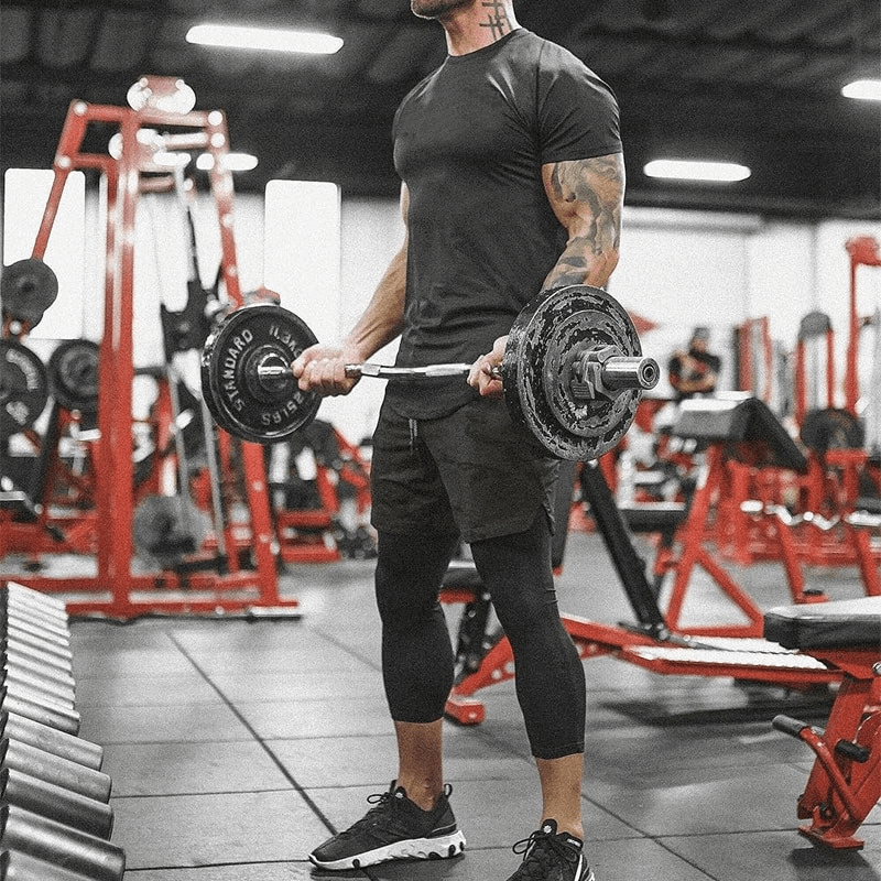 Man lifting weights in gym, wearing black athletic outfit, surrounded by red gym equipment.